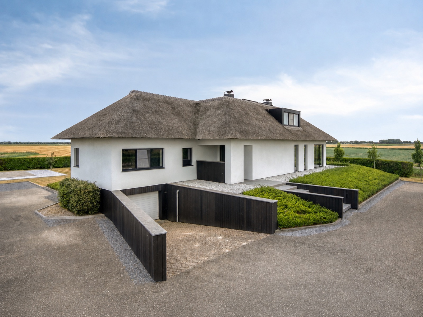 De villa vanaf de oprit, met rieten dak en aangelegde tuin
